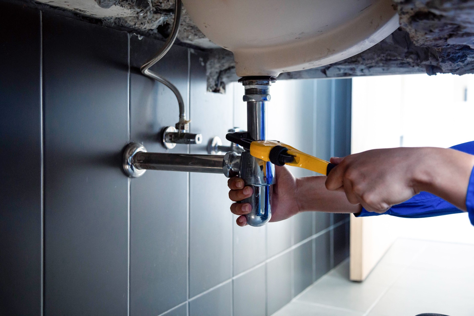 Plumber fixing white sink pipe with adjustable wrench.
